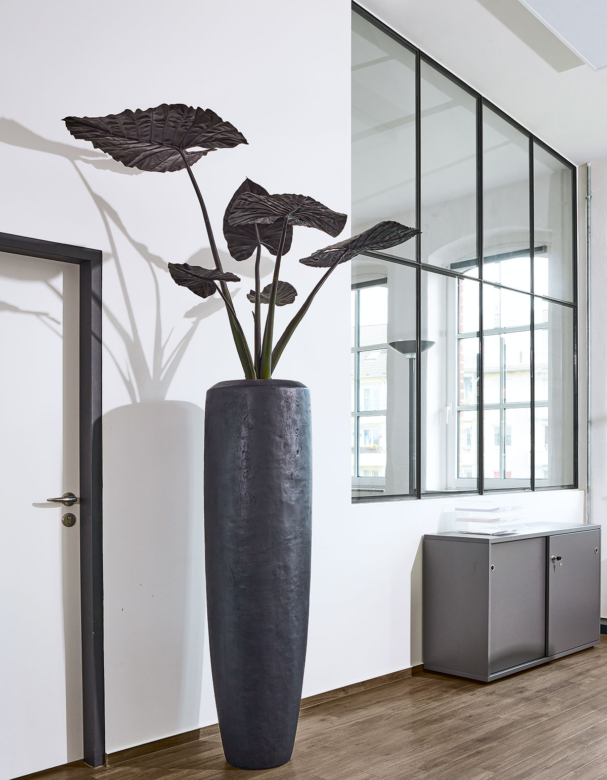 Variables Gefäßprogramm Links: Gefäß Loft XL mit einer Höhe von 1,5 ­Metern im Zusammenspiel mit einer nachgebildeten ­Alocasia, dunkel belaubt.