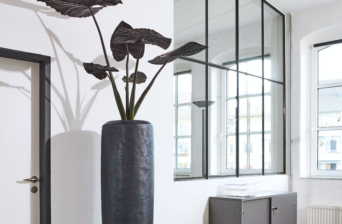  Variables Gefäßprogramm Links: Gefäß Loft XL mit einer Höhe von 1,5 Metern im Zusammenspiel mit einer nachgebildeten Alocasia, dunkel belaubt.